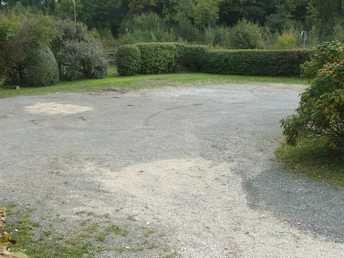 Kleiner Schotterparkplatz umgeben von dichter Vegetation, im Hintergrund dichte grüne Hecken.