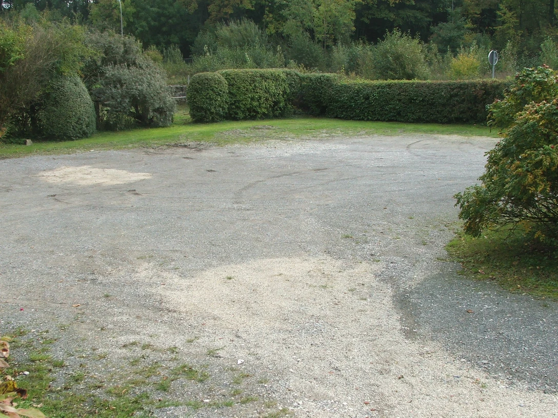 Parkplatz Hiddentrup Kleiner Schotterparkplatz umgeben von dichter Vegetation, im Hintergrund dichte grüne Hecken.