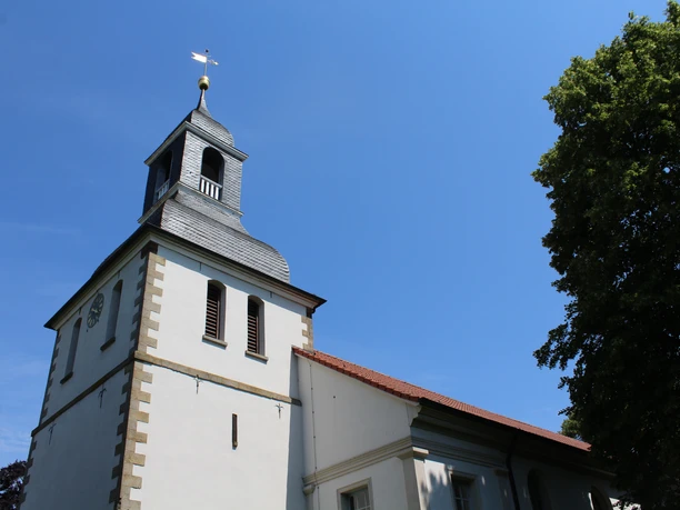 Eine schlichte Kirche mit Glockenturm in Thedinghausen, umgeben von Bäumen und blauem Himmel.