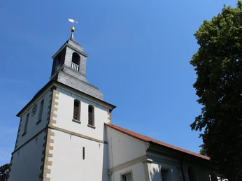 Thedinghausen Kirche Blender Eine schlichte Kirche mit Glockenturm in Thedinghausen, umgeben von Bäumen und blauem Himmel.