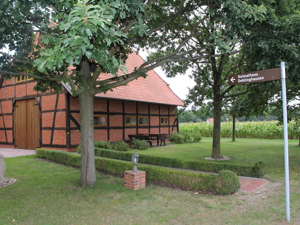 Half-timbered house with a red tiled roof, surrounded by trees, meadows and a signpost.
