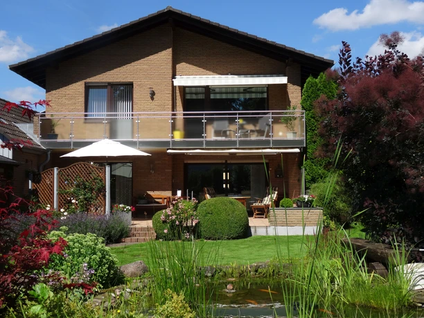 Ferienwohnung Kuhnert - Außenansicht Ferienwohnung in zweistöckigem Gebäude mit Balkon, Terrassenbereich und üppigem Garten inklusive Teich.