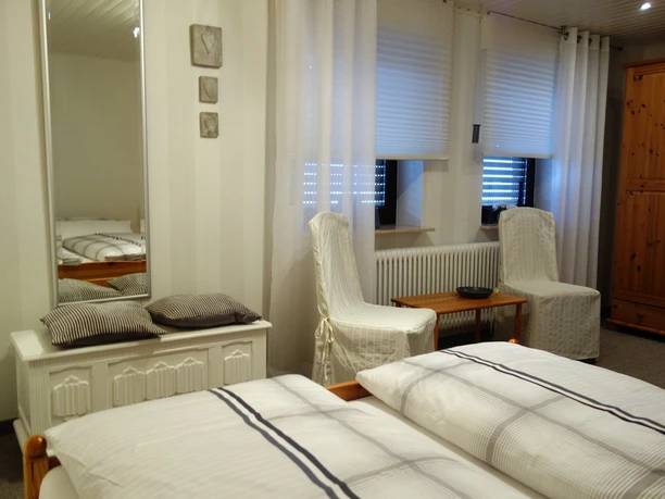 Ferienwohnung Kuhnert - Schlafzimmer Helles Schlafzimmer mit Doppelbett, zwei bequemen Sesseln, Holzmöbeln und einem großen Spiegel.