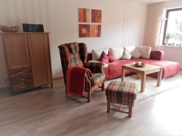 Ferienwohnung Kuhnert - Wohnbereich Gemütlicher Wohnbereich mit gemusterten Sesseln, rotem Sofa und Holzmöbeln auf hellem Laminatboden.