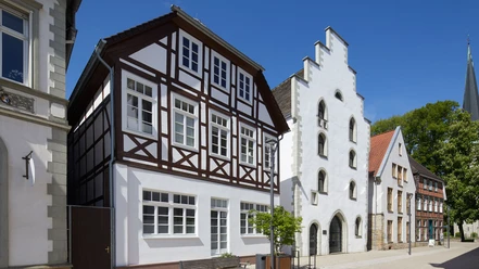 Historisches Fachwerkhaus und Giebelhaus aus weißem Putz im Sonnenschein, Teil eines Altstadtensembles.