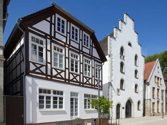 Historisches Fachwerkhaus und Giebelhaus aus weißem Putz im Sonnenschein, Teil eines Altstadtensembles.