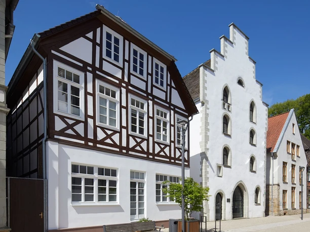 Historisches Fachwerkhaus und Giebelhaus aus weißem Putz im Sonnenschein, Teil eines Altstadtensembles.