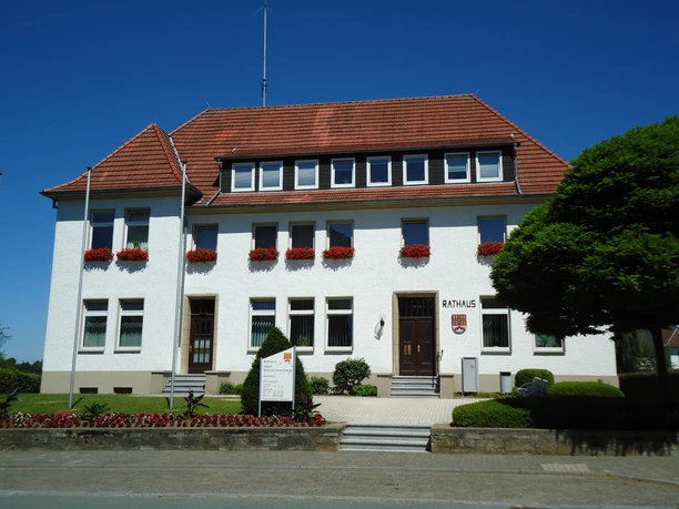 Rathaus Bad Wünnenberg Das weiße, zweistöckige Rathaus von Bad Wünnenberg mit roten Dachziegeln und blühenden Blumenkästen.