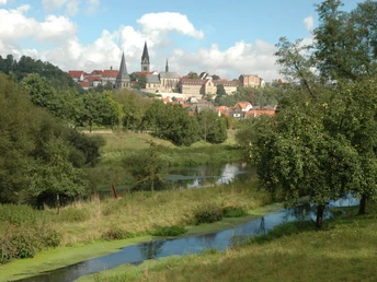 Südansicht Warburg Blick über eine grüne Landschaft mit Fluss auf die historische Silhouette von Warburg unter blauem Himmel.