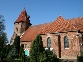 St. Laurentius Kirche Die St. Laurentius Kirche mit roter Backsteinfassade und spitzem Turmdach, umgeben von Bäumen.St. Laurentius Church with its red brick façade and pointed tower roof, surrounded by trees.Laurentius-kirken med sin røde murstensfacade og spidse tårntag, omgivet af træer.De Sint-Laurentiuskerk met zijn rode bakstenen gevel en spitse torendak, omringd door bomen.