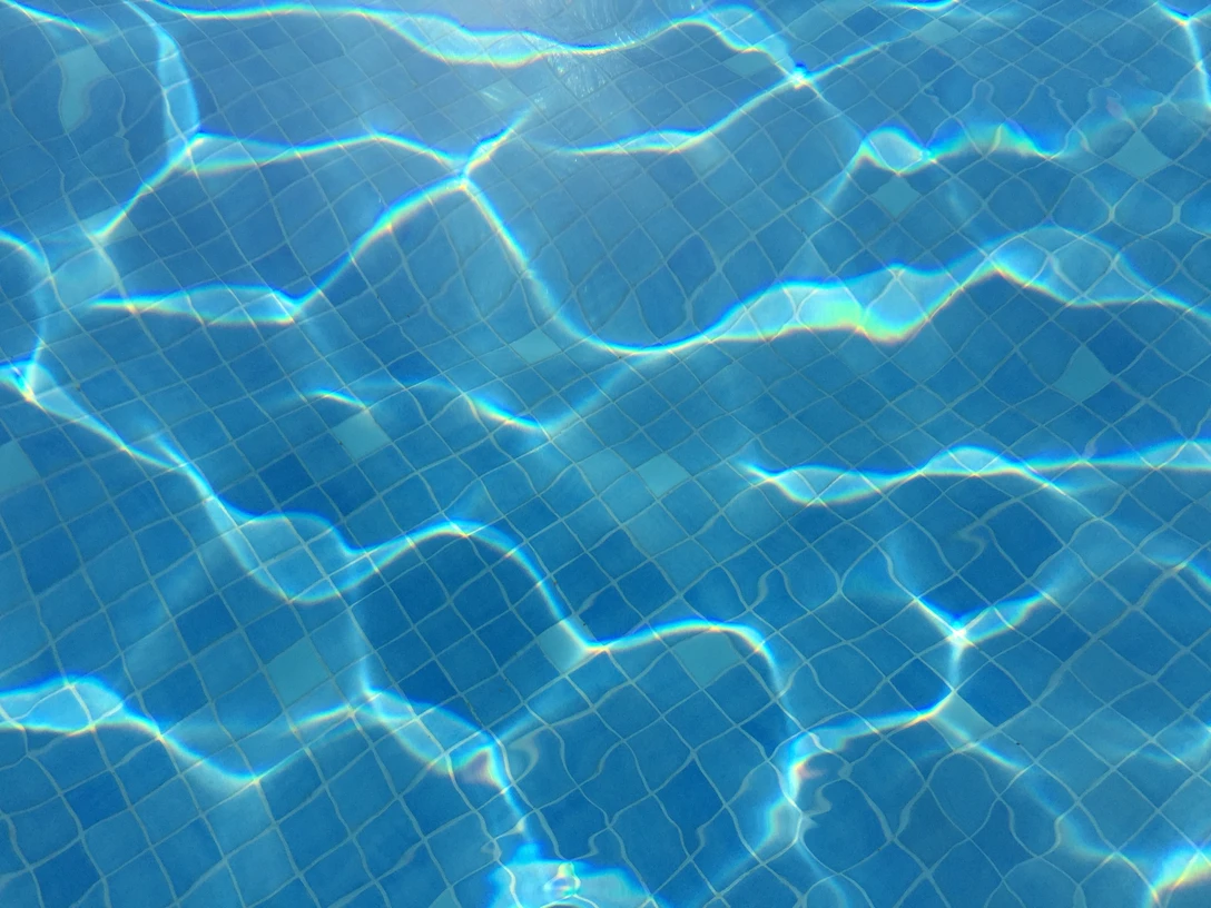 Klares, blaues Wasser eines Schwimmbeckens mit sanften Lichtreflexionen auf gefliester Oberfläche.Clear, blue water of a swimming pool with gentle light reflections on a tiled surface.Klart, blåt vand i en swimmingpool med blide lysrefleksioner på en flisebelagt overflade.Helder, blauw water van een zwembad met zachte lichtreflecties op een betegeld oppervlak.