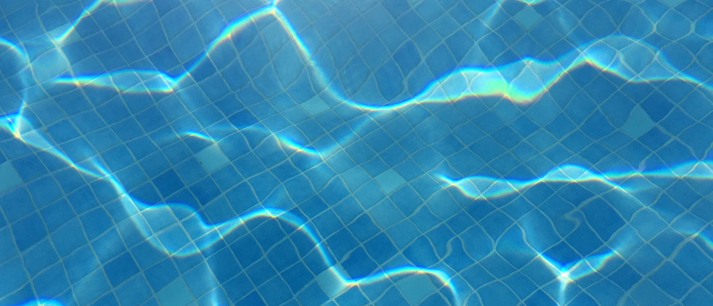 Schwimmbecken Klares, blaues Wasser eines Schwimmbeckens mit sanften Lichtreflexionen auf gefliester Oberfläche.