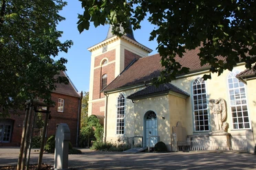 Kirche Uchte Eine historische Kirche mit gelber Fassade, großem Turm und mehreren Rundbogenfenstern.