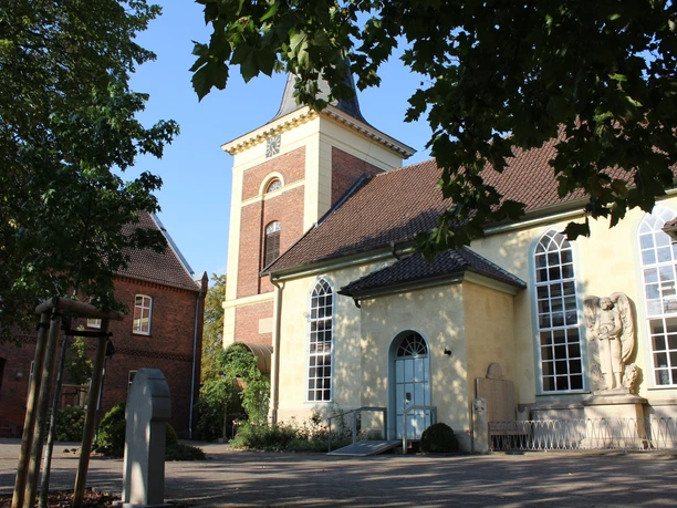 Kirche Uchte Eine historische Kirche mit gelber Fassade, großem Turm und mehreren Rundbogenfenstern.