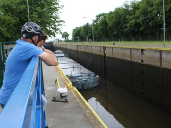 Ein Mann mit Fahrradhelm beobachtet auf einer Brücke eine Schleuse, in der ein Schlepper passiert.