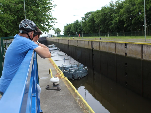Schleuse Langwedel Ein Mann mit Fahrradhelm beobachtet auf einer Brücke eine Schleuse, in der ein Schlepper passiert.