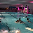 Schwimmbecken mit abendlicher Beleuchtung, Bademöglichkeiten und einige Menschen beim Schwimmen.