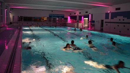 Hallenbad in Brakel Schwimmbecken mit abendlicher Beleuchtung, Bademöglichkeiten und einige Menschen beim Schwimmen.