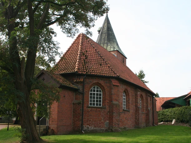 Brick church with a red tiled roof, situated by a tree, surrounded by a well-tended lawn.