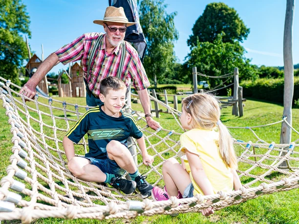 Ludowinengarten in Bökendorf Zwei Kinder spielen fröhlich auf einem Kletternetz im Ludowinengarten, begleitet von einem älteren Mann.