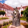 Kloster auf der Brede, Brakel Klostergelände mit Bronzeskulptur einer jungen Frau und eines Kindes, umgeben von historischen Gebäuden.