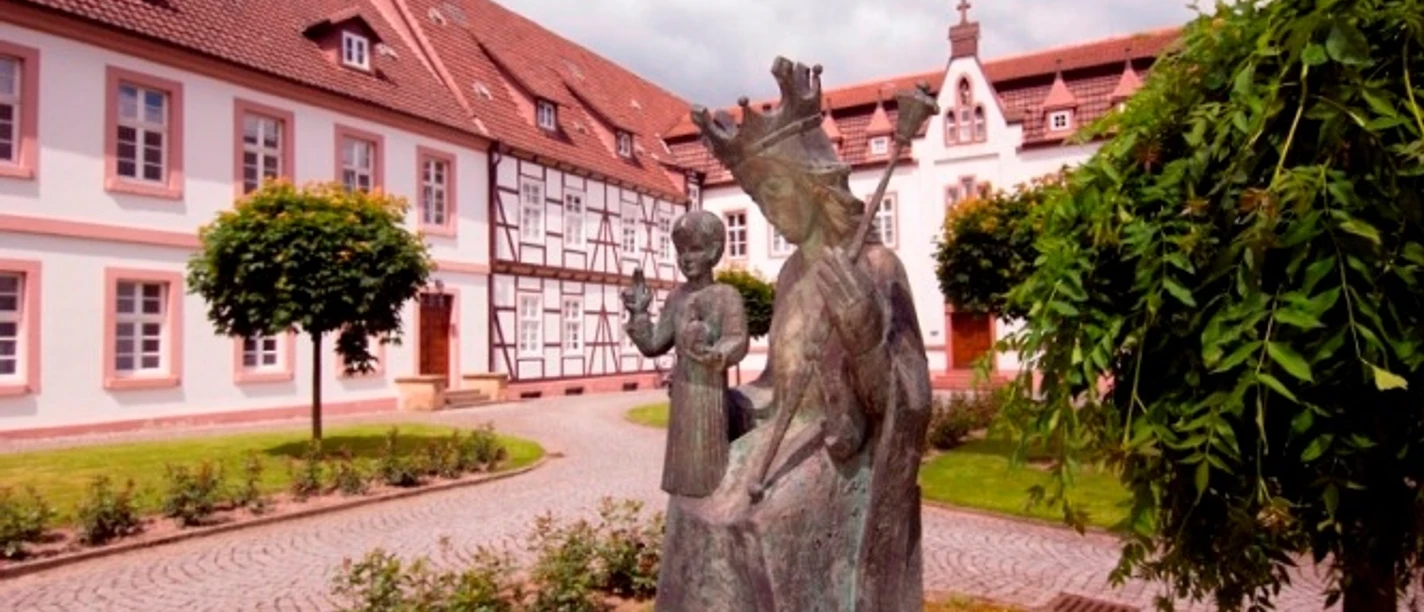 Kloster auf der Brede, Brakel Klostergelände mit Bronzeskulptur einer jungen Frau und eines Kindes, umgeben von historischen Gebäuden.