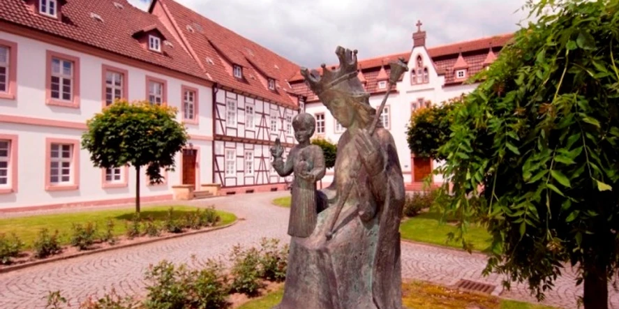 Kloster auf der Brede, Brakel Klostergelände mit Bronzeskulptur einer jungen Frau und eines Kindes, umgeben von historischen Gebäuden.