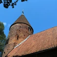 Kirche St. Annen Westen Backsteinkirche mit markantem Rundturm und Schieferdach, umgeben von Bäumen und blauem Himmel.