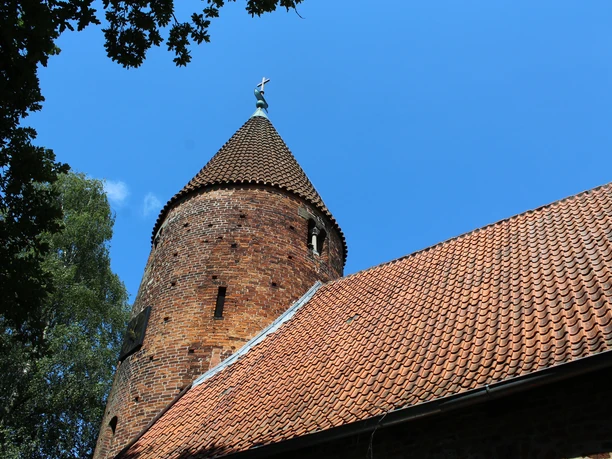 Kirche St. Annen Westen Backsteinkirche mit markantem Rundturm und Schieferdach, umgeben von Bäumen und blauem Himmel.