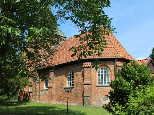 The round-brick church in Binnen, with its red roof, stands against a bright blue sky and is surrounded by trees.