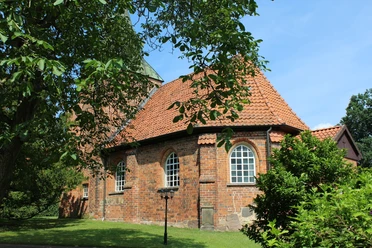 Kirche Binnen Rundziegelbau der Kirche Binnen mit rotem Dach vor einem strahlend blauen Himmel und umgeben von Bäumen.