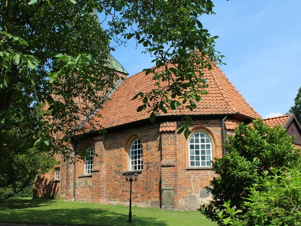Kirche Binnen Rundziegelbau der Kirche Binnen mit rotem Dach vor einem strahlend blauen Himmel und umgeben von Bäumen.