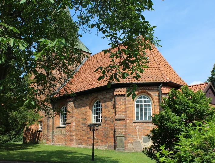 Kirche Binnen Rundziegelbau der Kirche Binnen mit rotem Dach vor einem strahlend blauen Himmel und umgeben von Bäumen.