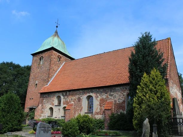 Historische Backsteinkirche mit markantem Turm und begrüntem Umfeld unter blauem Himmel.