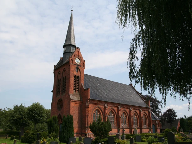 Historische Backsteinkirche St. Georg mit hohem Turm, umgeben von grünem Friedhof und Bäumen.