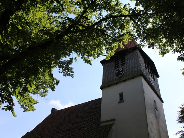 Kirche Raddestorf Die Kirche in Raddestorf mit ihrem markanten Uhrturm, eingebettet in das grüne Blätterdach der Bäume.