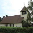 Kirche in Essern mit markantem Glockenturm, umgeben von Bäumen und von einer Hecke eingefasst.