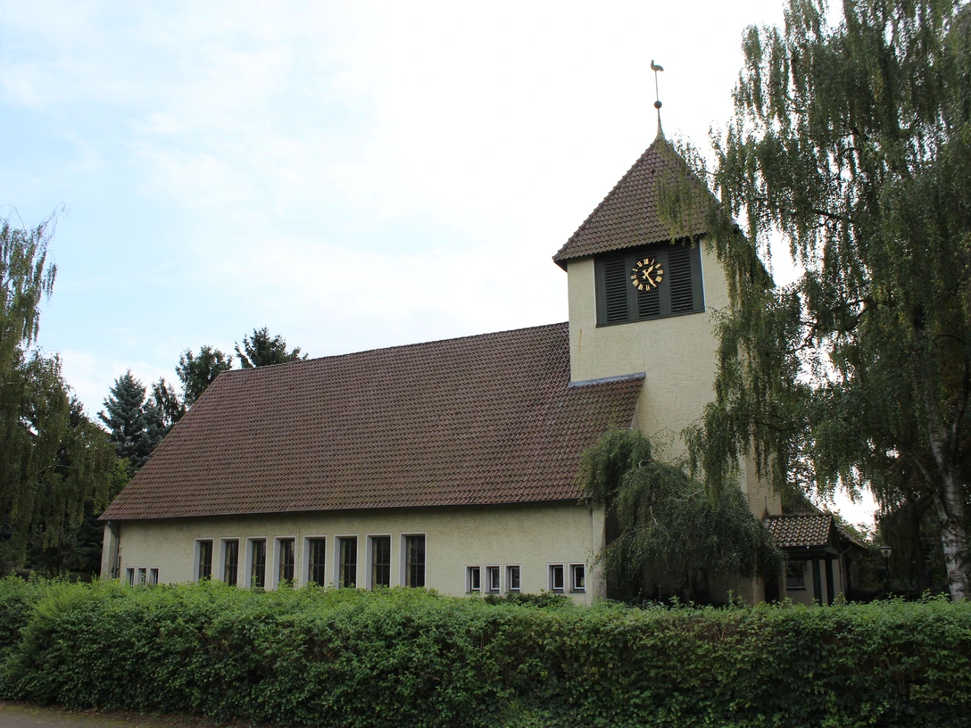 Kirche Essern Kirche in Essern mit markantem Glockenturm, umgeben von Bäumen und von einer Hecke eingefasst.