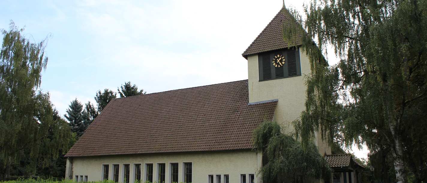 Kirche Essern Kirche in Essern mit markantem Glockenturm, umgeben von Bäumen und von einer Hecke eingefasst.