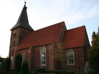 Gotische Backsteinkirche mit rotem Satteldach und Turm mit spitzem Helm im Abendlicht.