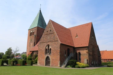 Kirche Riede Backsteinkirche mit grünem Turmdach, Satteldächern und gepflegtem Grün vor blauem Himmel.