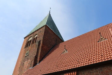 Kirche Riede mit rotem Ziegeldach und markantem grünen Kirchturm unter blauem Himmel.