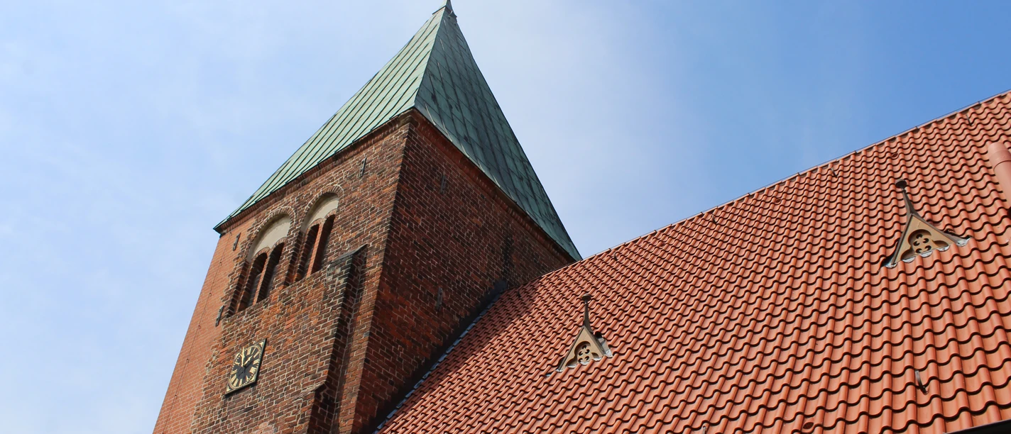 Kirche Riede mit rotem Ziegeldach und markantem grünen Kirchturm unter blauem Himmel.