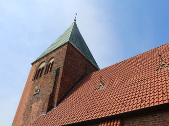 Kirche Riede mit rotem Ziegeldach und markantem grünen Kirchturm unter blauem Himmel.