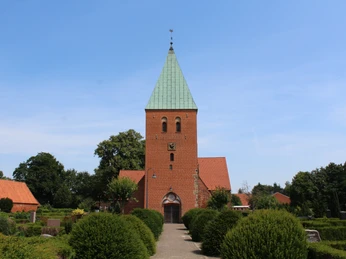 Historische Backsteinkirche mit grünem Turmdach, umgeben von gepflegter Gartenlandschaft.