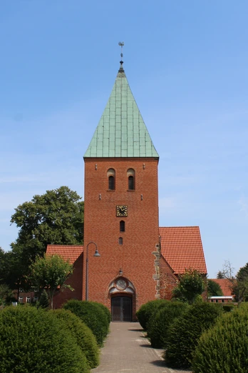 Kirche Riede Historische Backsteinkirche mit grünem Turmdach, umgeben von gepflegter Gartenlandschaft.