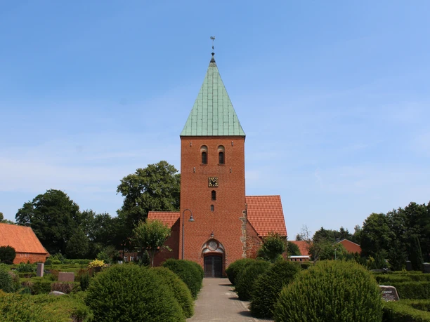 Kirche Riede Historische Backsteinkirche mit grünem Turmdach, umgeben von gepflegter Gartenlandschaft.