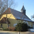 Historische Kirche mit gelbem Anstrich und markantem Holzturm, umgeben von Bäumen im Winter.