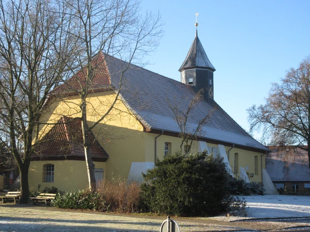 Historische kerk met gele verf en opvallende houten toren, omringd door bomen in de winter.