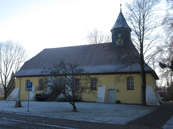 Ehemalige St. Jacobi-Kirche in Husum mit gelber Fassade, kleinem Türmchen und schneebedeckten Bäumen.